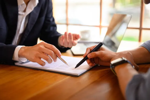 Two people at a table going over a document together, one pointing out a line with a pen.