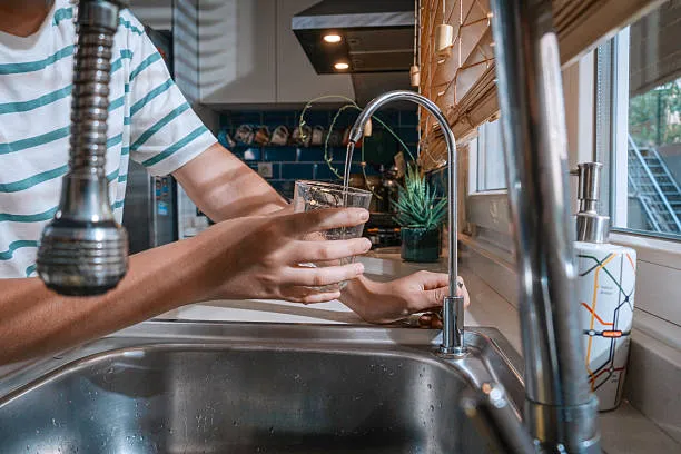 A glass being filled from a dedicated reverse osmosis faucet mounted beside a kitchen sink.