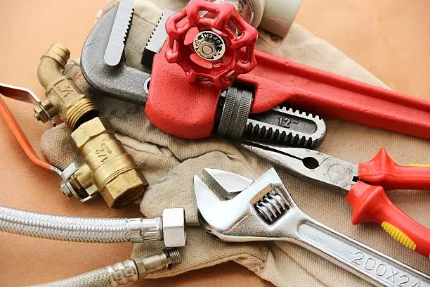 Pipe wrench, adjustable wrench, shut-off valve and braided supply line laid out on a work cloth.