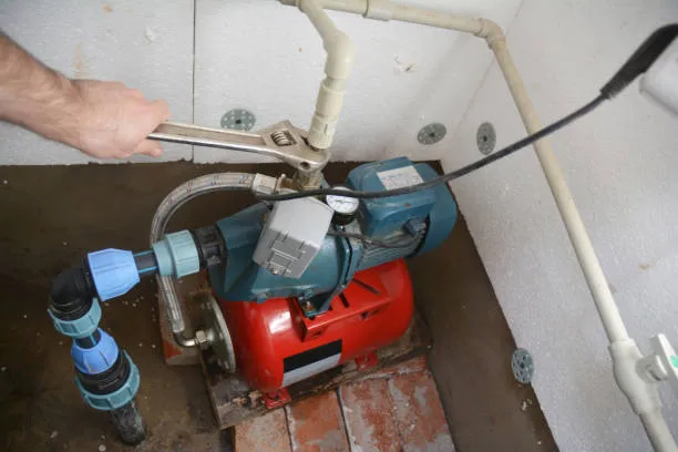 A well pump and pressure tank in a utility space, with a pressure gauge and a wrench on the fitting above it.